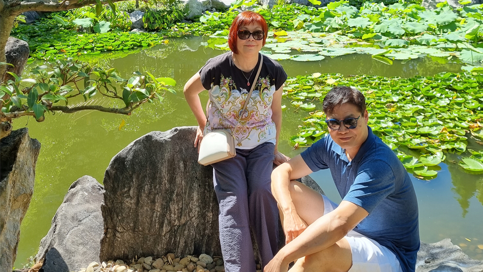 A photo of Yen and Vincent in front of greenery with Vincent perching on a rock.